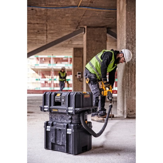 A DEWALT DCV586MT2 portable vacuum and tool storage unit is positioned on a construction site floor, with two workers in