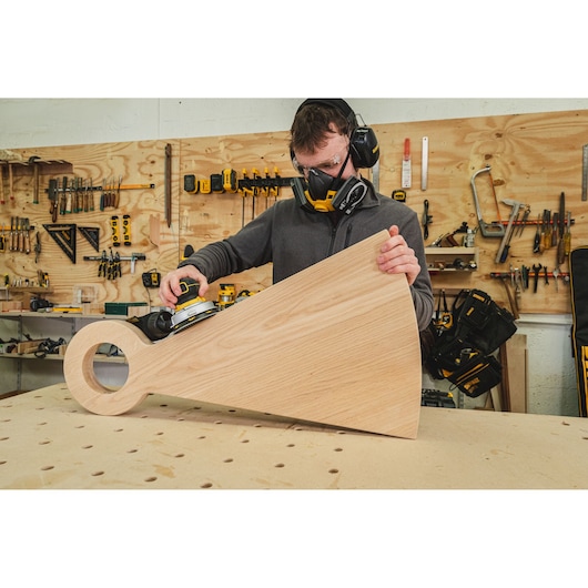 Person using a DEWALT sander on a large wooden piece in a workshop.