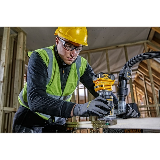 Worker using DEWALT DCW604 router on wood, wearing safety gear in a construction site.