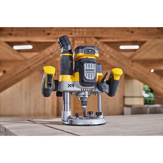 A DEWALT cordless router with yellow and black accents is displayed on a wooden workbench in a workshop setting.