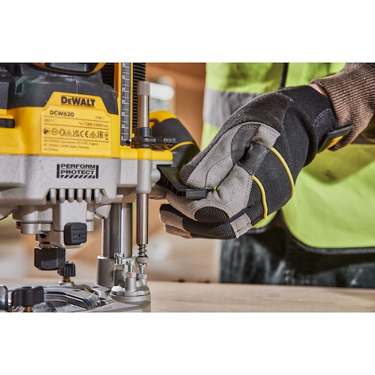 Close-up view of a person wearing work gloves and a safety vest operating a DEWALT DCW620 power tool, adjusting its parts on a wooden surface.
