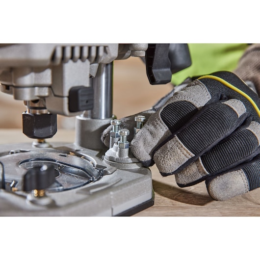 Close-up of a gloved hand adjusting bolts on a metallic DEWALT power tool mounted on a wooden surface.