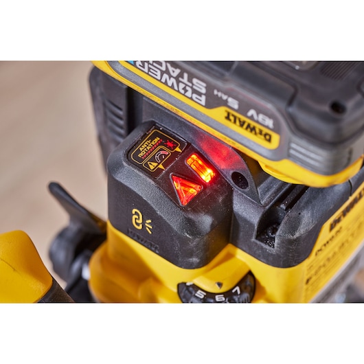 Close-up view of a DEWALT PowerStack battery attached to a yellow power tool, showing indicator lights and warning labels.