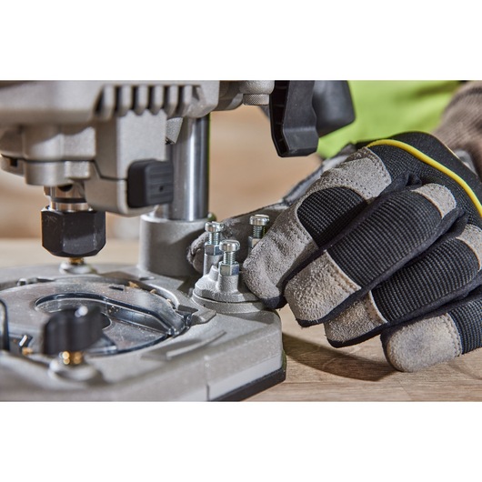 Close-up of a gloved hand adjusting bolts on a DEWALT power tool, positioned on a wooden surface.