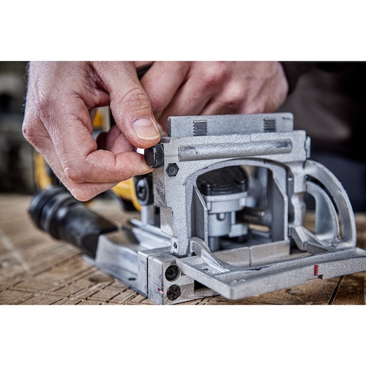 Close-up of a person adjusting a knob on a DEWALT jointer tool, showing detailed metal components on a woodworking surface.