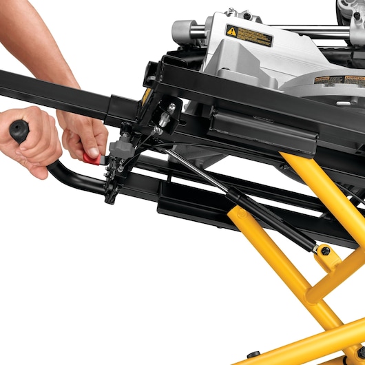 Close-up view of a DEWALT DE7260 photography equipment stand being adjusted by a person's hands. The image shows the sturdy yellow and black metal frame and adjustment mechanism.