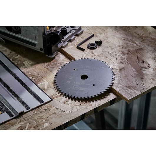 A DEWALT circular saw blade with fine teeth is placed on a wooden workbench, alongside a power tool, a metal ruler, an allen key, and small hardware components.