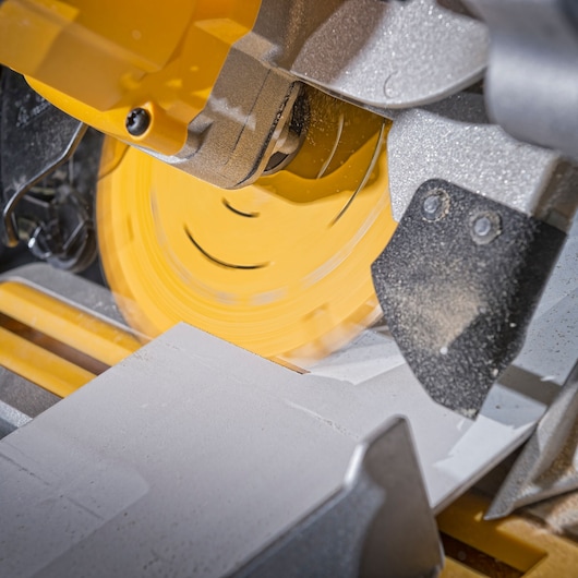 Close-up of a yellow circular saw cutting through a piece of material, with visible sawdust and motion blur from the spinning blade.