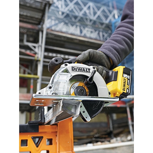 DEWALT cordless circular saw cutting metal at a construction site, operated by a person wearing gloves.