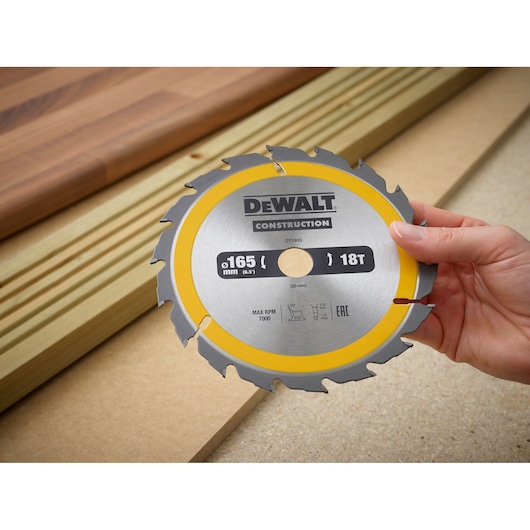 A hand holds a DEWALT DT1933 165mm circular saw blade, shown above wooden boards.