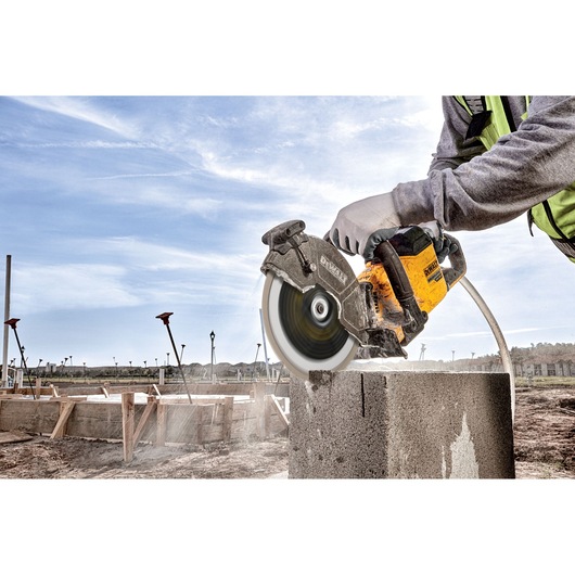 A person wearing work gloves uses a DEWALT power saw to cut through a concrete block at a construction site outdoors.