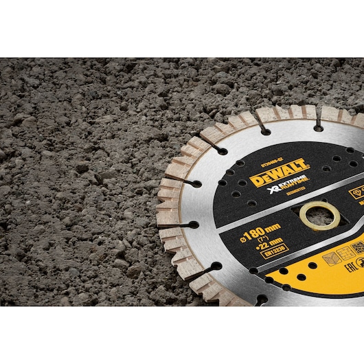 A DEWALT segmented diamond saw blade, model DT20468, partially visible and placed on a rough concrete surface. The blade features technical specifications including a diameter of 180 mm and a bore size of 22 mm, designed for extreme cutting performance.