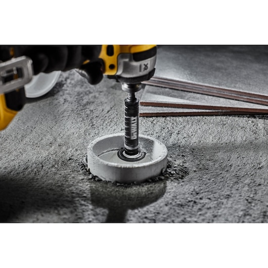 Close-up of a DEWALT drill with a hole saw cutting into concrete, with several metal rods visible in the background.