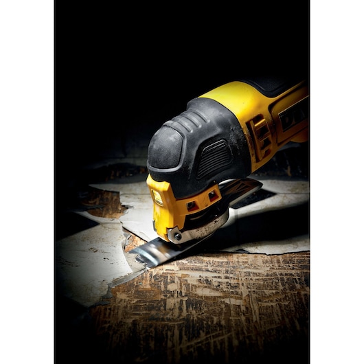 DEWALT oscillating multi-tool cutting through old flooring in a close-up, showing tool detail and action.