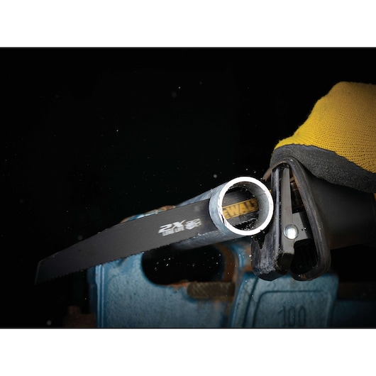 DEWALT saw blade cutting a metal pipe held in a blue vise, with a yellow-gloved hand operating the tool.