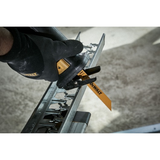 A close-up image of a gloved hand using a DEWALT reciprocating saw blade to cut through a piece of metal framing.