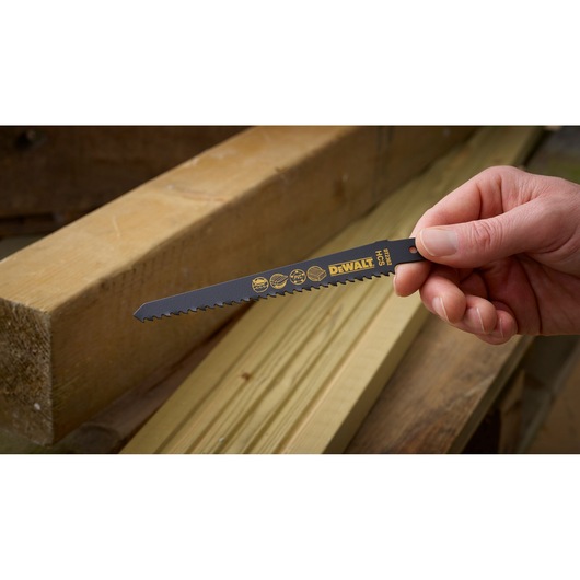 Hand holding a DEWALT DT2362 saw blade, placed near wooden planks in a workshop setting.