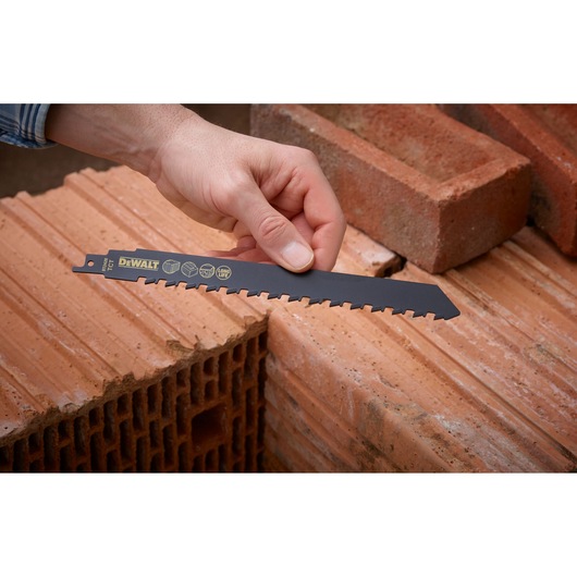 Hand holding a DEWALT DT2420 saw blade above stacked bricks, showcasing its use for masonry cutting.