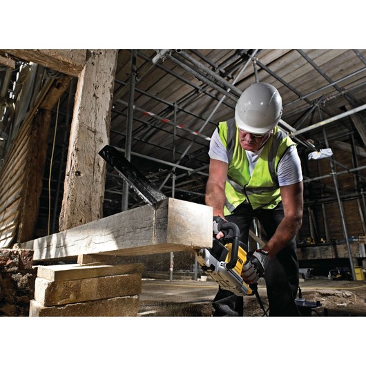 Worker uses DEWALT saw to cut wood beam at a construction site, wearing safety gear and a hi-vis vest.