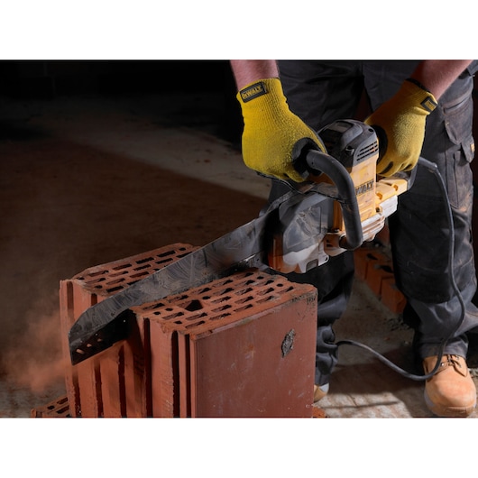 Person using a DEWALT saw to cut through red bricks, wearing yellow gloves and work boots.