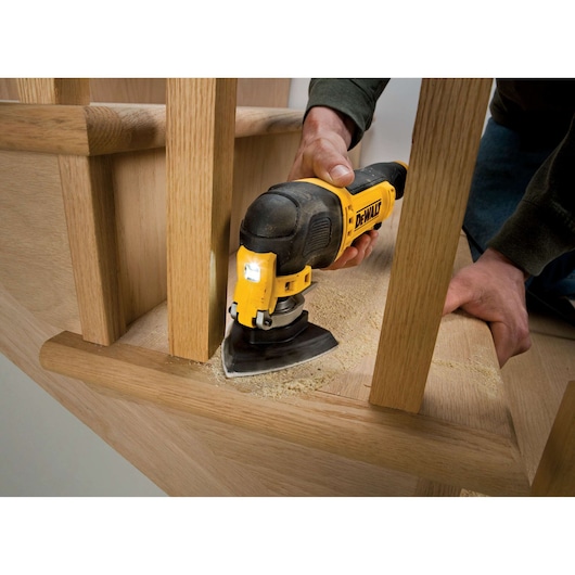 DEWALT oscillating tool sanding wood near stairs, held by person, producing sawdust.