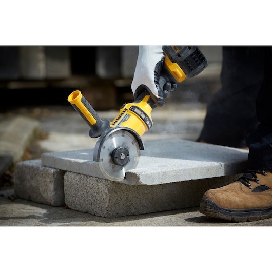 A DEWALT hand-held power tool cutting through a concrete slab, operated by a person wearing gloves and work boots.
