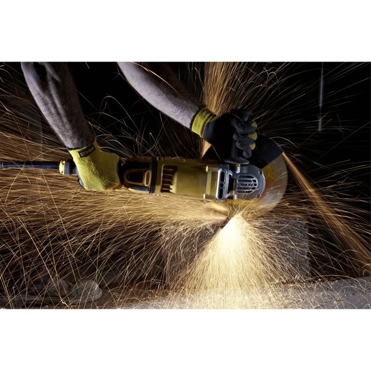 A person uses a DEWALT angle grinder, producing bright sparks while cutting material, wearing protective gloves.