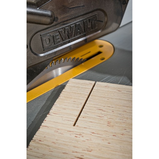 Close-up of a DEWALT table saw with a piece of wood being cut. The saw blade is partially visible and there is a straight cut in the wood.