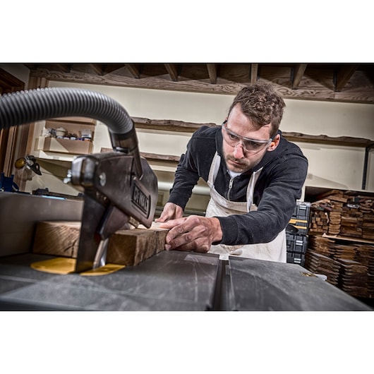 Person using a DEWALT machine to cut wooden planks in a workshop; face blurred for privacy.