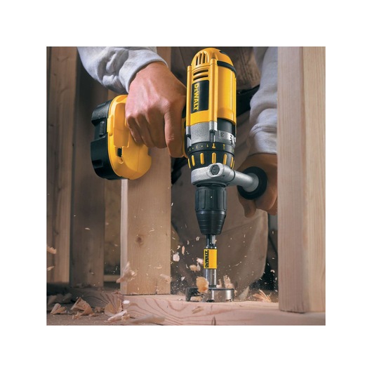 A DEWALT drill with DT4577 bit is used to drill a hole in wood, creating wood shavings and dust.