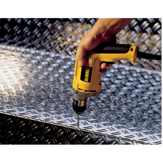 A yellow DEWALT electric drill is being used to drill into a textured metal surface.