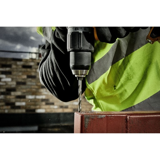 Close-up of gloved hand using a DEWALT drill to drill into metal, person in high-visibility jacket.