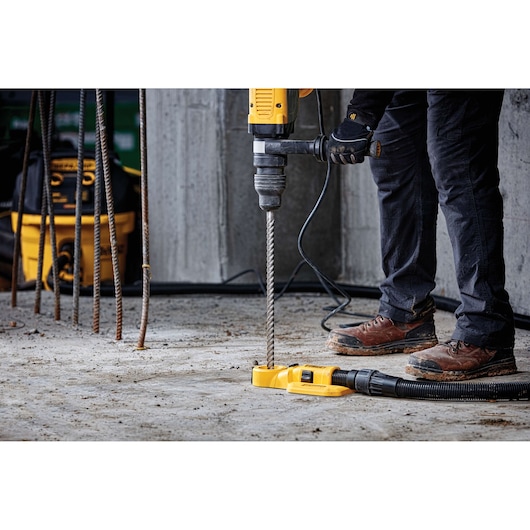 Person using a DEWALT drill with a dust extractor to drill into concrete at a construction site.