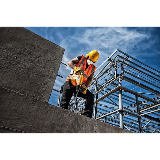 Construction worker using a yellow DEWALT tool on concrete with steel framework and blue sky in the background.