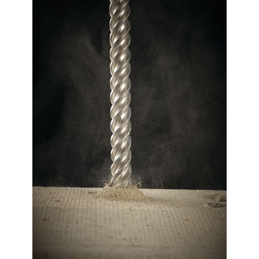 Close-up of a metallic spiral drill bit penetrating a concrete surface, releasing dust.