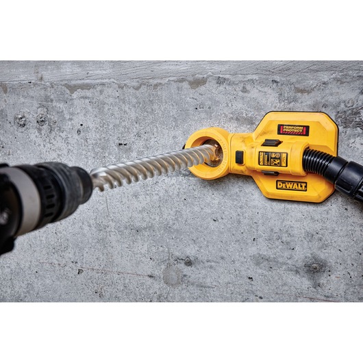 A DEWALT dust extraction attachment is being used with a rotary hammer drill to drill into a concrete wall. The attachment collects dust while drilling, helping to keep the workspace clean.