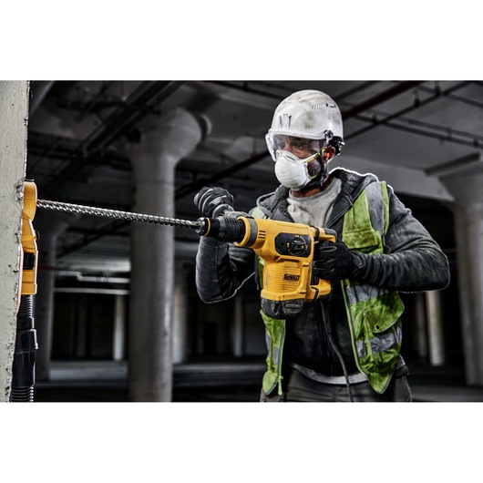 Worker uses DEWALT rotary hammer drill with DT60828 bit on concrete at a construction site.