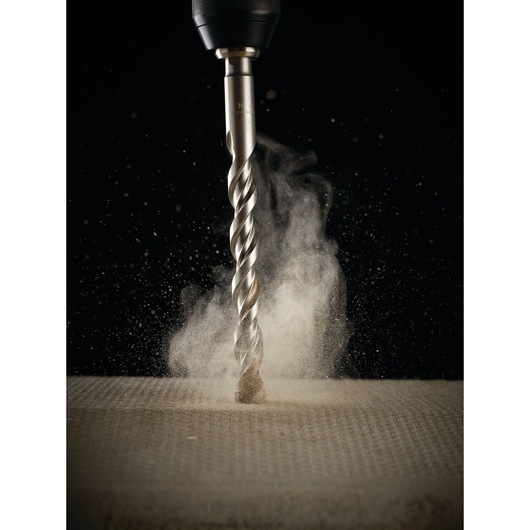 Close-up of a DEWALT drill bit making dust while drilling into a concrete surface.