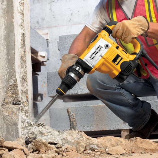 DEWALT DT6824 rotary hammer drill breaking concrete at construction site. Worker wears gloves and safety vest.
