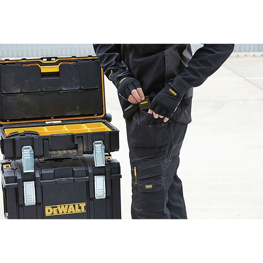 DEWALT tool storage box open with compartments, person in work gear stands nearby outdoors.