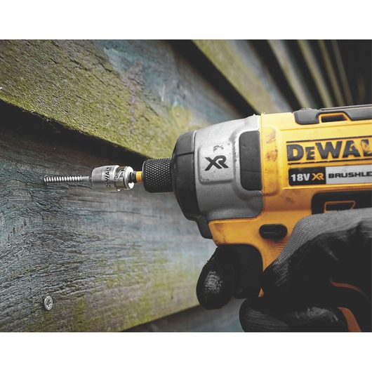 DEWALT cordless drill driving a screw into wood siding, close-up of tool and gloved hand.