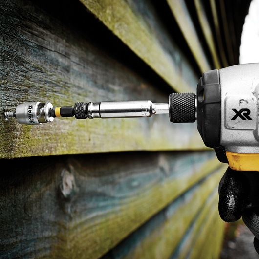 DEWALT drill with DT70537T accessory driving a screw into wooden planks outdoors.
