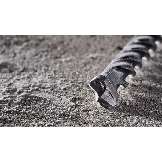 Close-up of a DEWALT DT8918 masonry drill bit lying on a gray, sandy surface, showing its pointed tip and spiral design.
