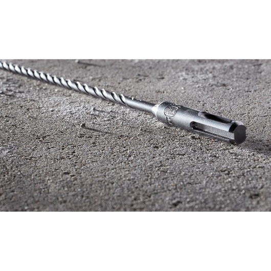 A close-up view of a DEWALT DT8923 masonry drill bit lying on a rough concrete surface.