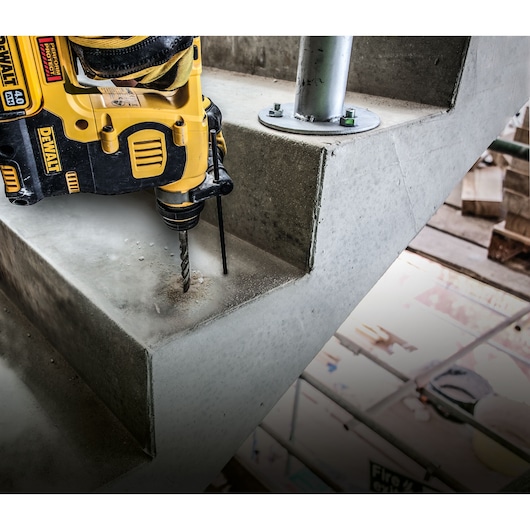 A DEWALT cordless drill is being used to drill into a concrete staircase at a construction site.