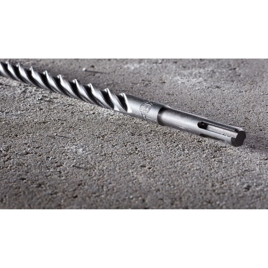 A close-up view of a DEWALT DT8936 rotary hammer drill bit with an SDS-plus shank, lying on a rough concrete surface.