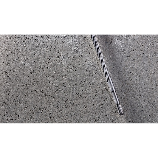 A close-up of a DEWALT masonry drill bit partially inserted into a rough concrete surface.