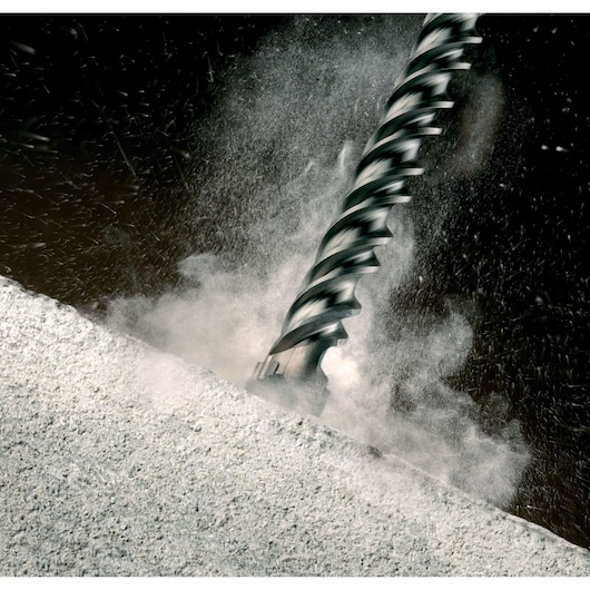 Close-up of a DEWALT rotary hammer drill bit (SKU: DT9400) drilling into a concrete surface, with dust and debris being emitted as the bit penetrates the material.