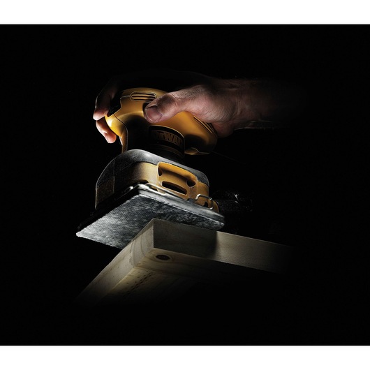 Hand using a DEWALT sander on a wooden plank in low light.