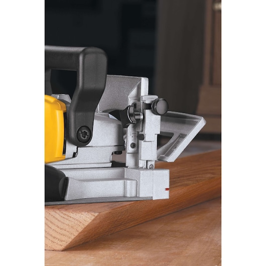 Close-up of a DEWALT DW682K biscuit joiner being used to cut a slot into a piece of wood, showing the tool's metal housing and adjustment knobs.